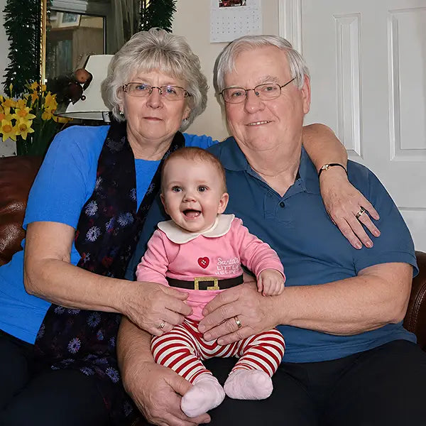 Deceased grandparents added to a photo, holding their baby granddaughter on the sofa